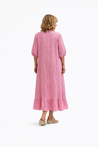 Vestido largo de lino rosa con botones frontales, mangas con volumen y volante en el bajo. Modelo de espaldas